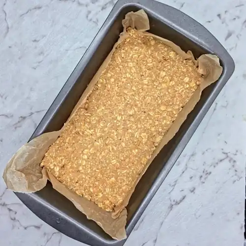  Press the chickpea mixture into the baking paper lined loaf pan. Chickpea mixture ingredients include rolled oats, oat flour, chickpeas, almond butter, coconut oil, maple syrup and vanilla extract. 