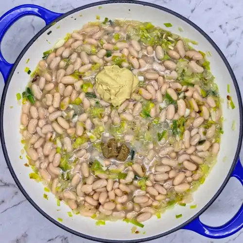 All the ingredients for Leeky Beans in a frying pan ready for gentle simmering. Leeks, onion, garlic, cannellini beans, stock cube and mustard.