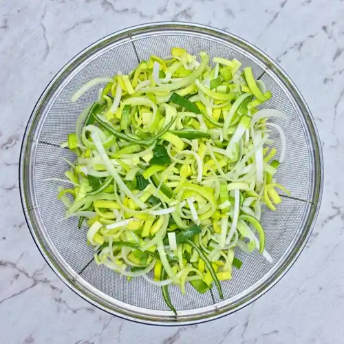 Leeks finely sliced and washed in a metal colander.