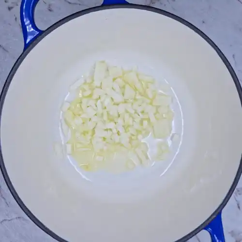 Finely chopped, raw onion and oil in a pot ready for frying.