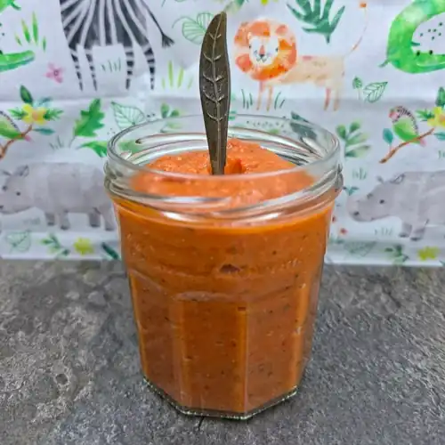Pureed Roasted Vegetable Tomato Sauce in a glass jar with a feather tipped serving spoon.