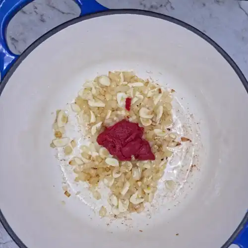 To the fried onions, add the sliced garlic and tomato paste. Pot.