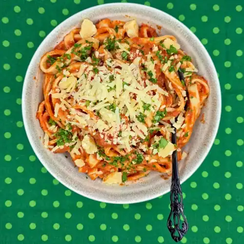 Ratatouille Pasta Sauce tossed through cooked, homemade pasta and topped with freshly grated parmesan cheese. Served in a bowl with a fork.