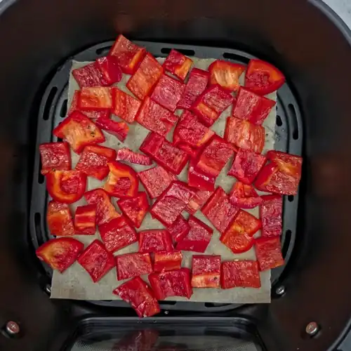 Chopped raw red capsicum tossed in oil, salt and pepper. Placed in a baking paper lined air fryer basket ready for roasting.